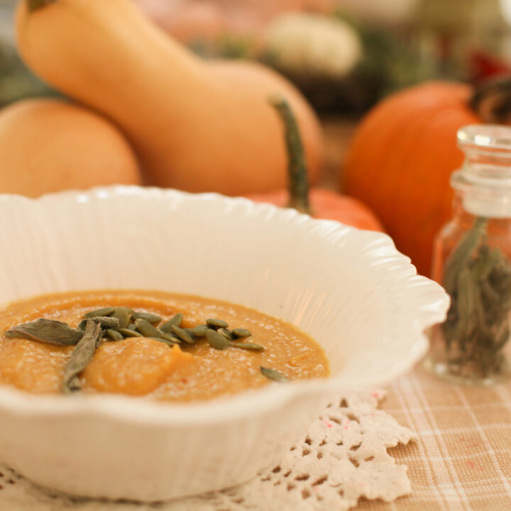 white bowl of pumpkin soup with pumpkin seeds and a bottle of sage