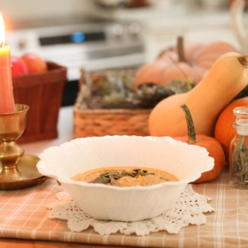 soup in white bowl next to candle and pumpkin