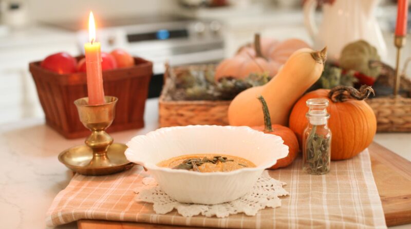 soup in white bowl next to candle and pumpkin